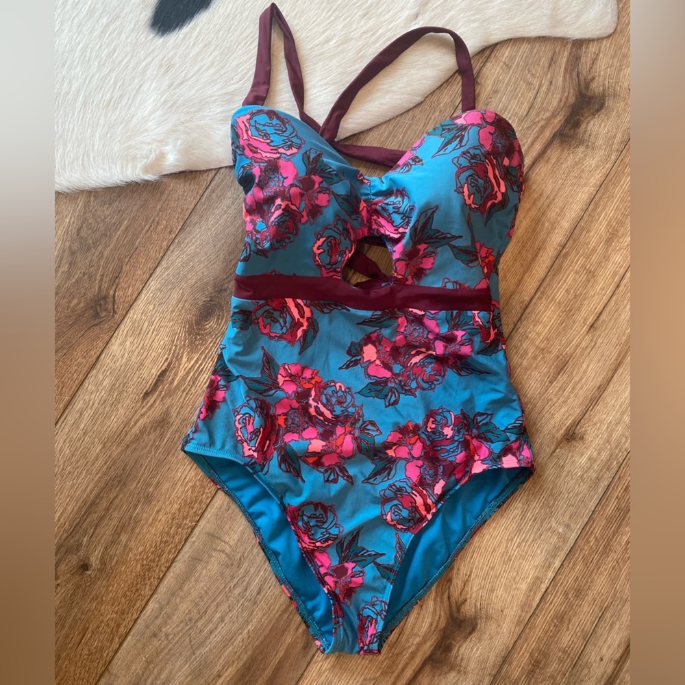 Basta Surf one-piece swimsuit with a teal background and a pink floral pattern